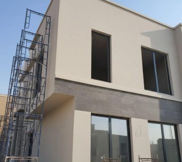 "تصميم واجهة فيلا مودرن بالدمام مقسومة لونين (بيج رملي ورمادي فاتح)، توضح فن تنسيق الاصباغ الخارجية والديكورات "