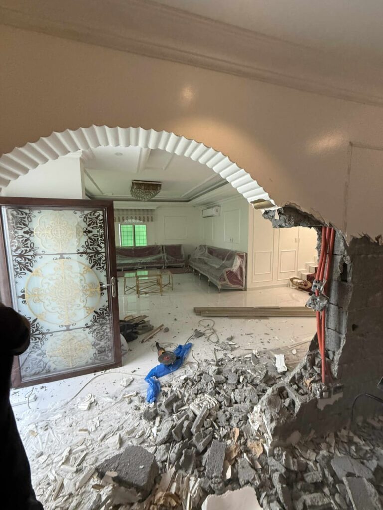"صورة لأعمال تكسير وتجديد داخل شقة: فتحة قوسية في الحائط مع ركام على الأرض وغرفة معيشة خلفها أثناء التشطيب "