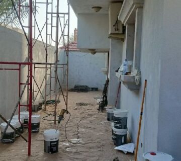 واجهة منزل تخضع لأعمال ترميم منازل الخبر وتشطيب منازل الظهران، وتظهر في الصورة السقالات وعلب الطلاء وأدوات مقاول ترميم منازل متخصص 