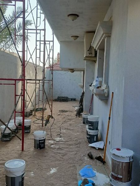 واجهة منزل تخضع لأعمال ترميم منازل الخبر وتشطيب منازل الظهران، وتظهر في الصورة السقالات وعلب الطلاء وأدوات مقاول ترميم منازل متخصص 
